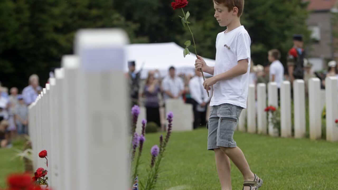 A child lays a flower on the gravestone of an Australian soldier