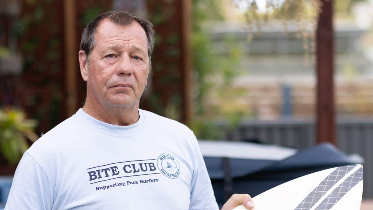 A man wearing a Bite Club t-shirt holds a surfboard