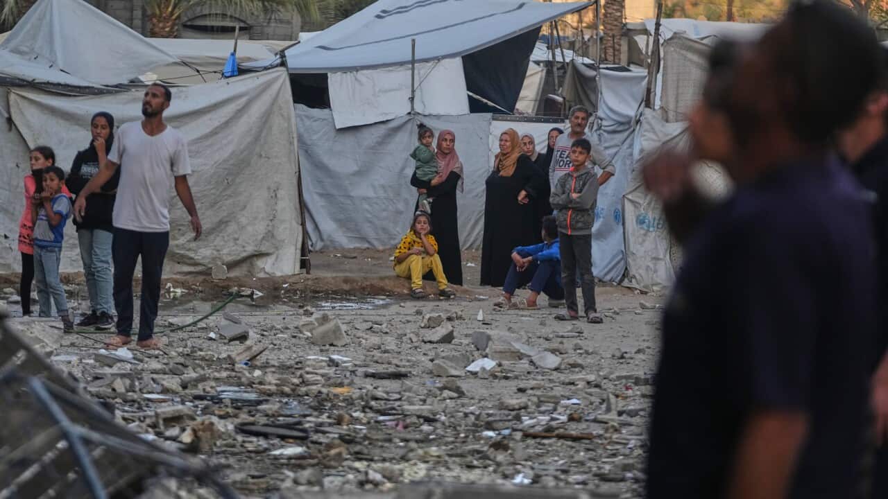 People standing amid rubble and tents.