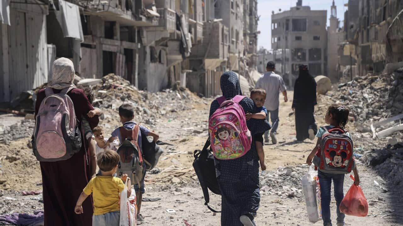A group of women and young children walk through rubble.