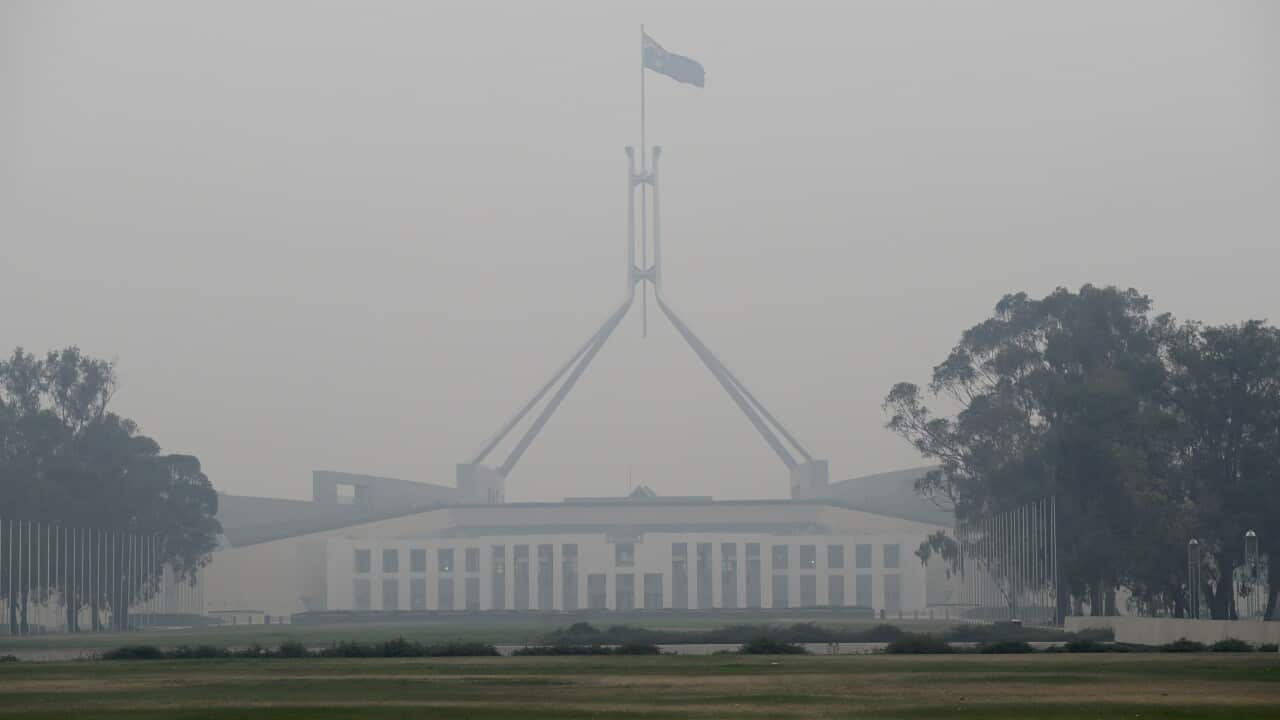 The Australian flag flies above Parliament House as smoke shrouds the capital.