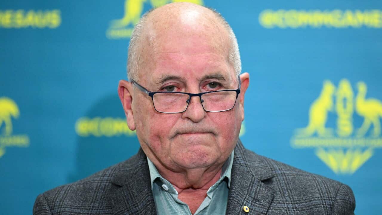 A man wearing glasses and a blazer, standing at a podium and listening.