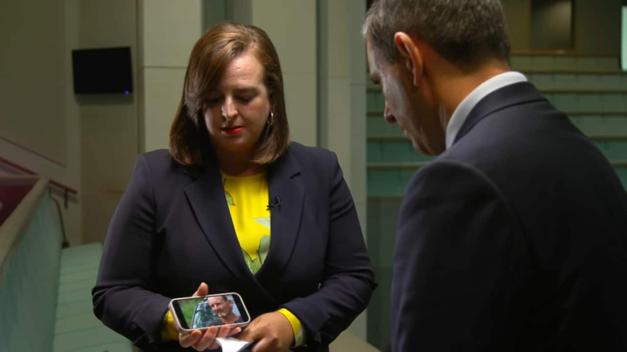 A woman and a man in a suit look down at a phone video