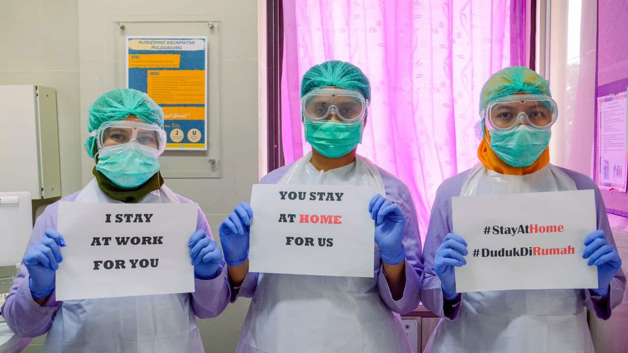 Medical workers wearing a face mask holds a 'Stay at Home' poster at a medical center in Jakarta, Indonesia.