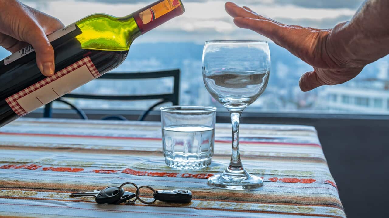 Hand of a man refusing red wine and showing car keys and a glass of water on a table at home