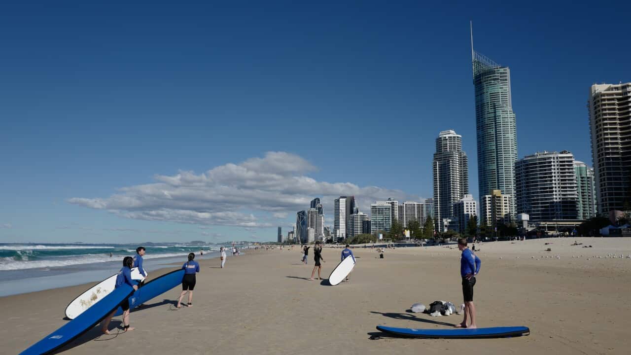 Surfers on a beach. There are high rise buildings in the background.