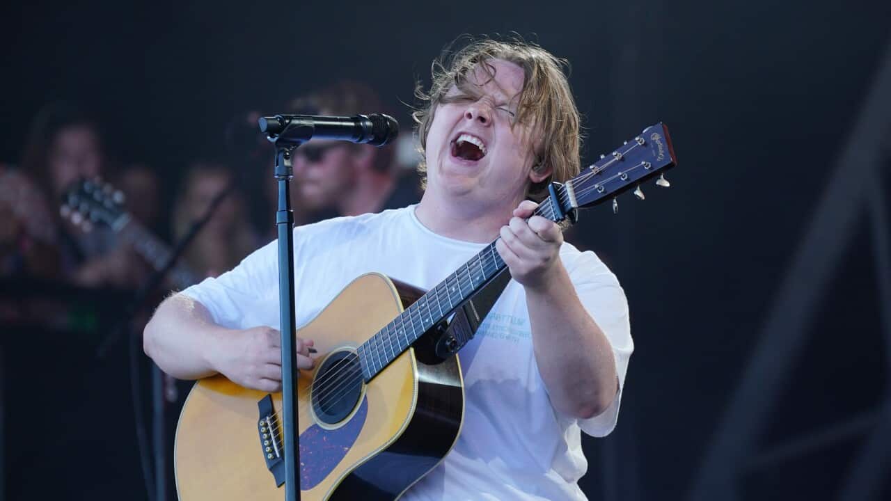 A man in a white t-shirt sings and plays an acoustic guitar