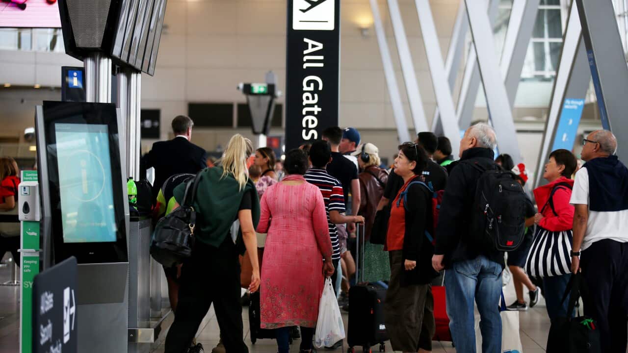 travellers waiting next to the 'All gates' sign at an airport