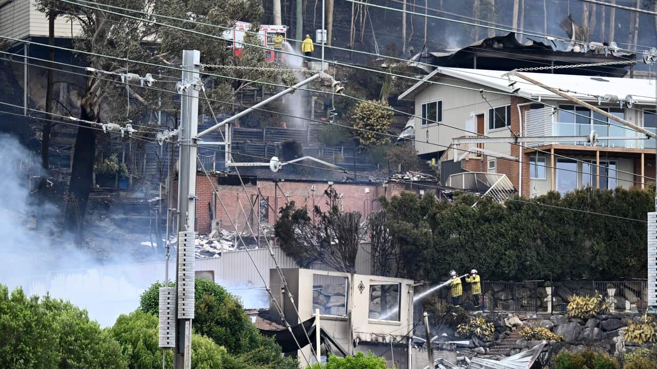 Damage from a bushfire as emergency workers can be seen hosing down buidilngs.