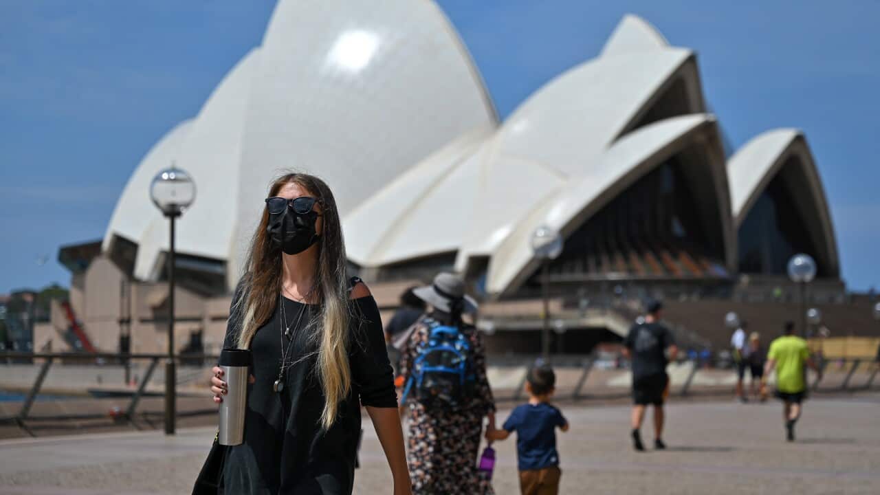 People wearing masks walk in front of the Sydney Opera House at Circular Quay in Sydney.