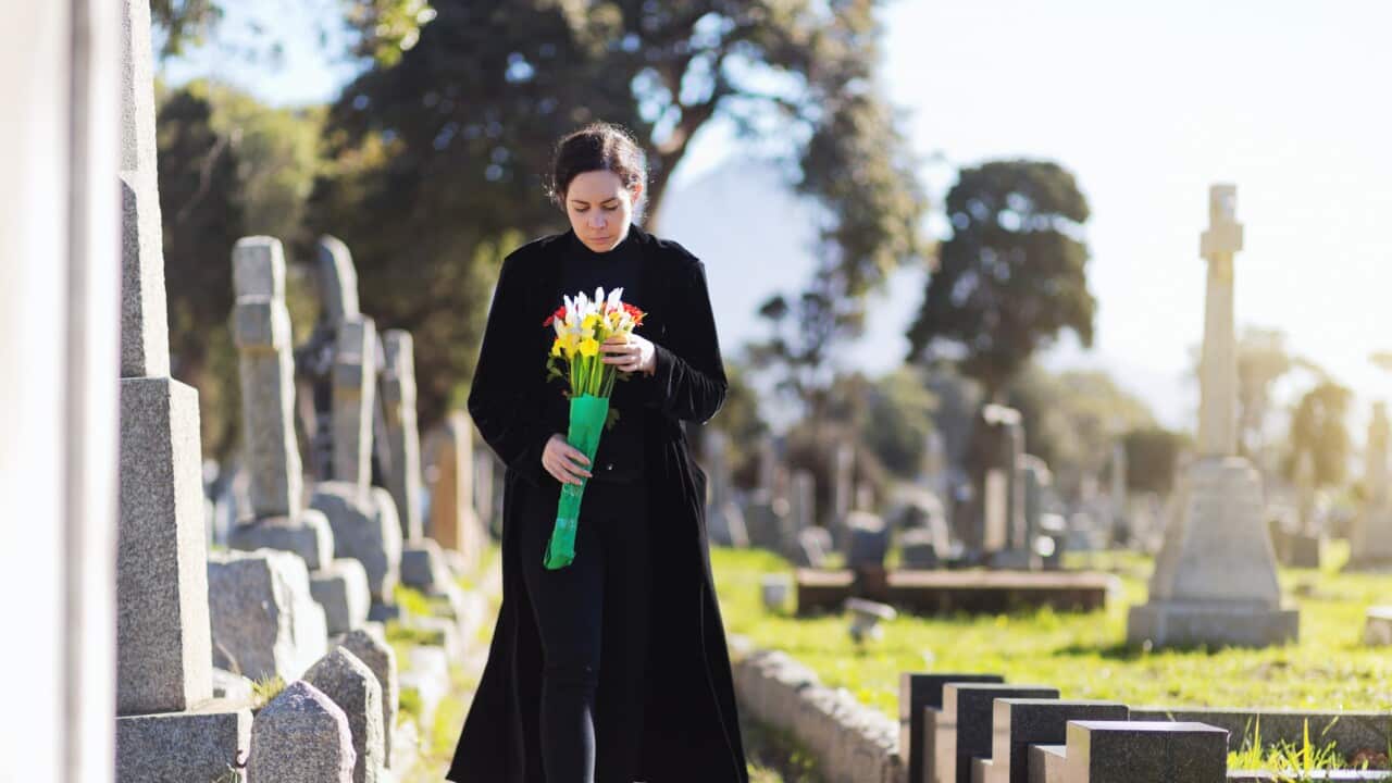 Bereaved young woman in black taking flowers to grave