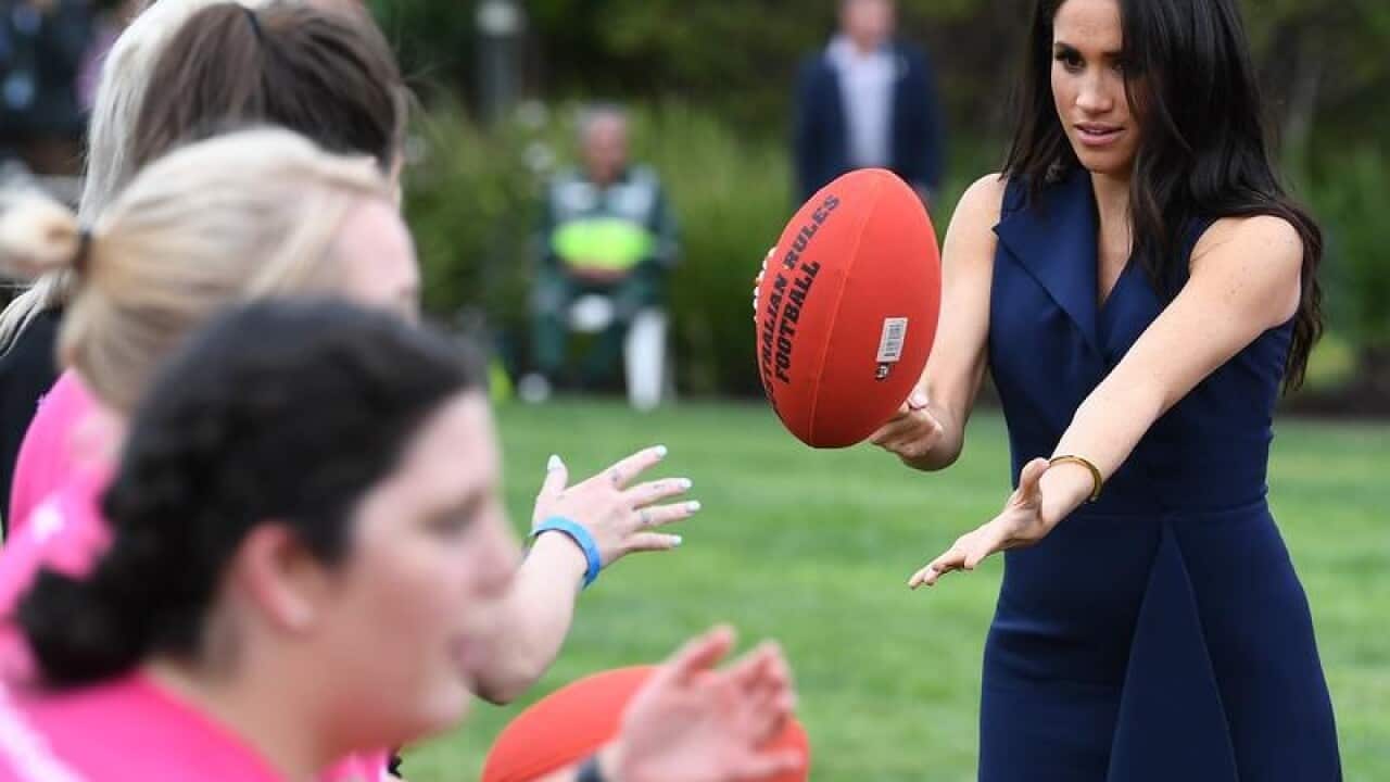 The Duchess of Sussex handballs an Australian Rules football.