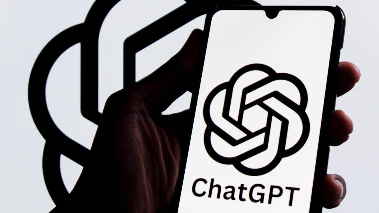 A hand holding a phone in front of a screen showing the OpenAI logo