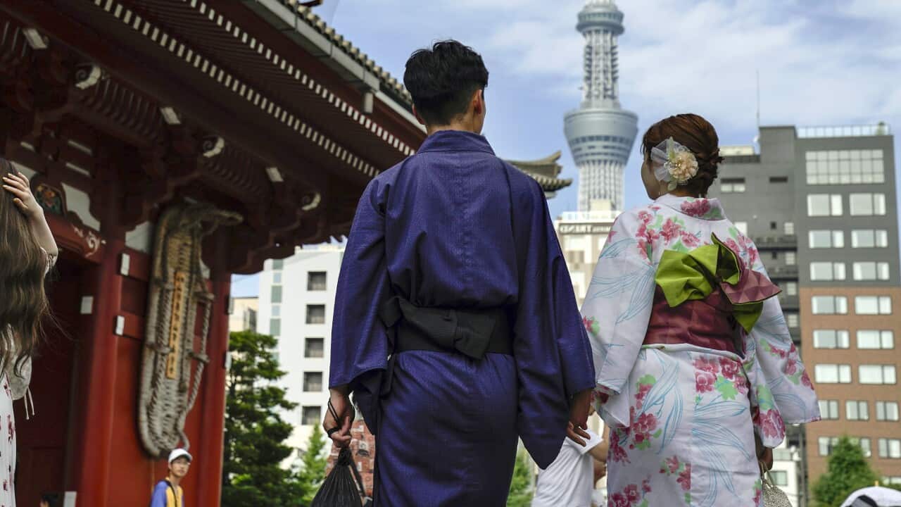 A couple wearing kimono's holds hands as they walk into a temple.