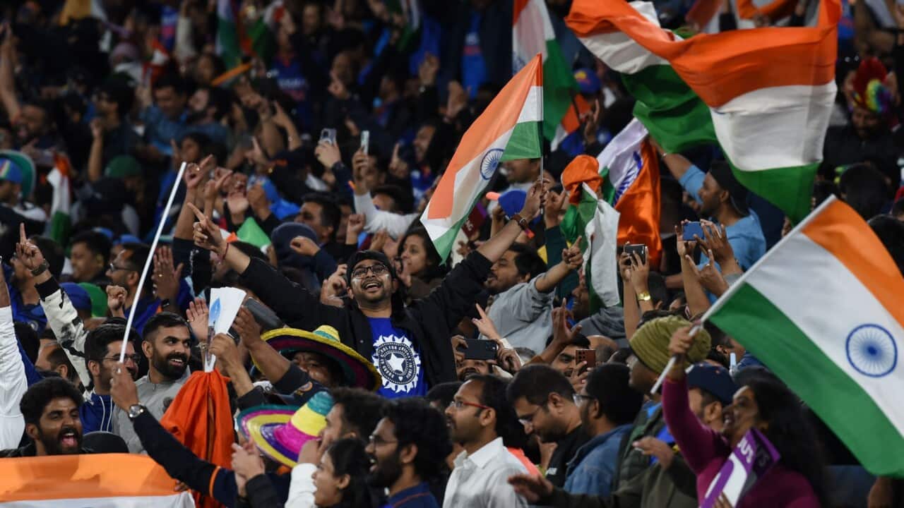 A section of a crowd at the cricket. A number of people are waving Indian flags