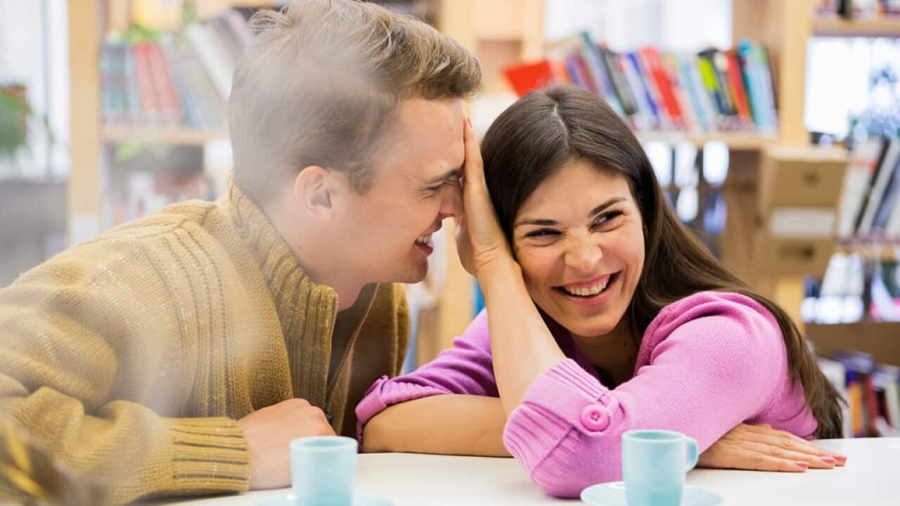 Playful young couple with coffee cups on desk in library