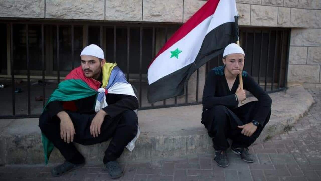 Members of the Druze community of the Israeli-annexed Golan Heights sit holding the Syrian and their community's flag (Getty Image)