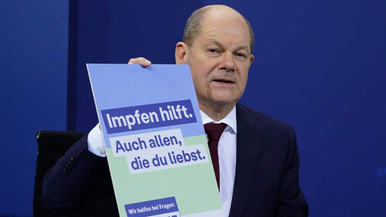 German Chancellor Olaf Scholz holds sign saying 'vaccination helps'