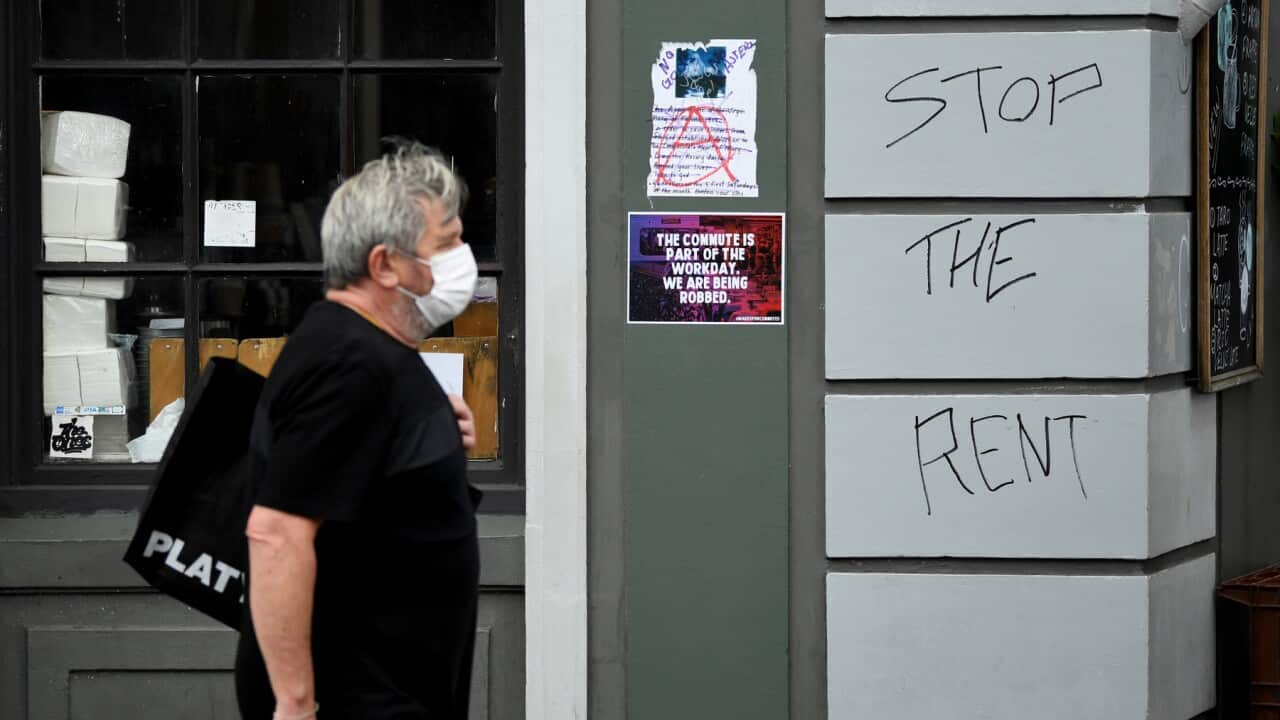 Man walks past a shop with 'Stop the Rent' graffiti.