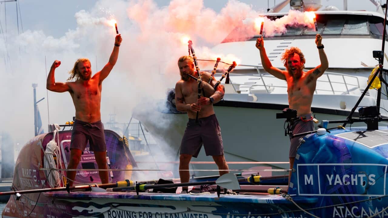Three men standing on a boat, letting off flares. One is playing the bagpipes.