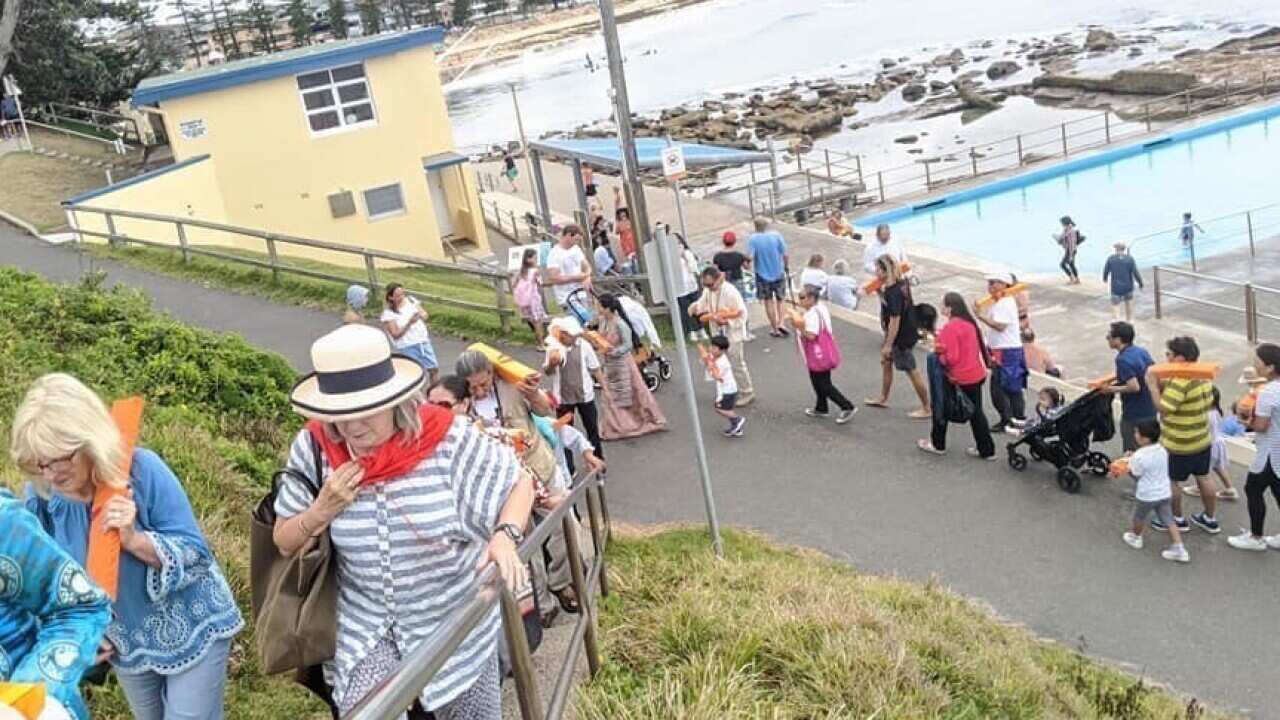 Tibetans circumambulate carrying Buddhist scripture at Dee Why beach, Northern Beaches