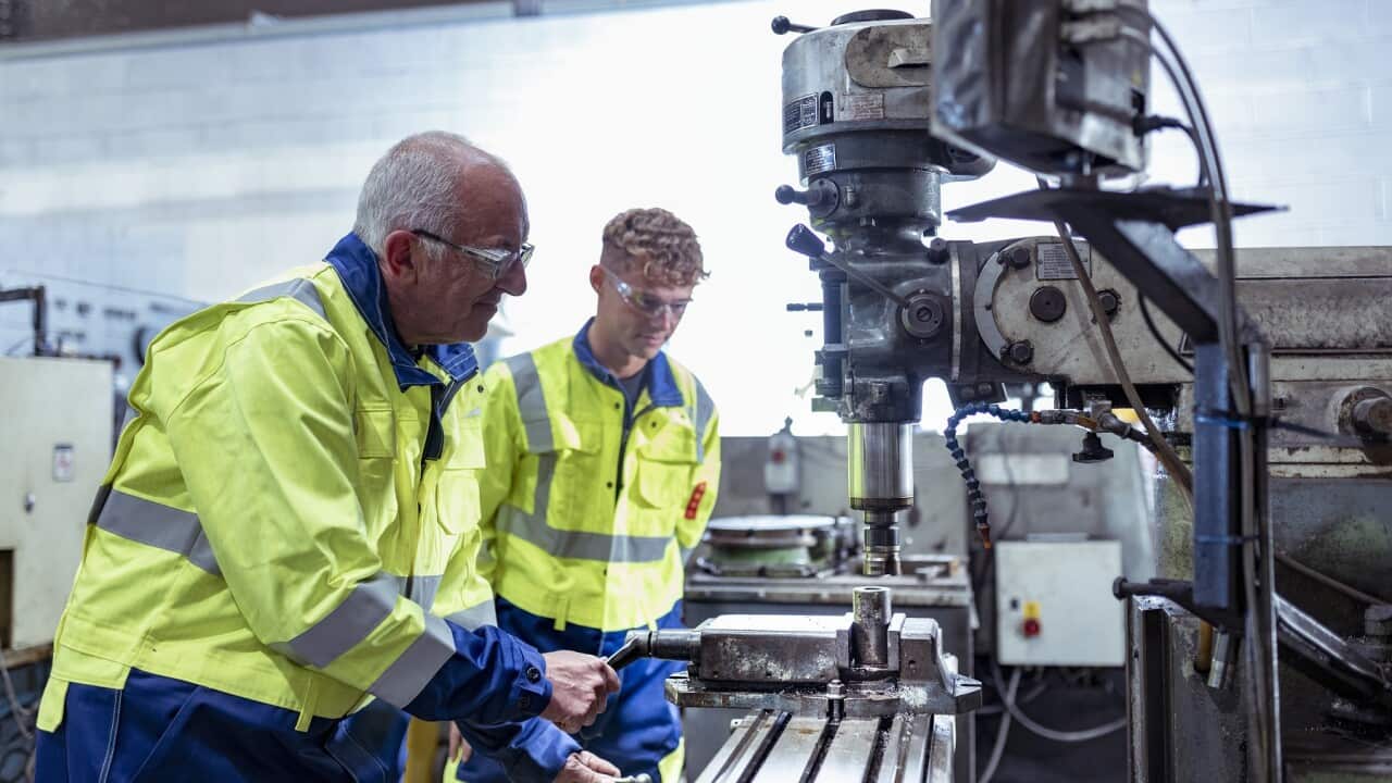 Engineer mentoring apprentice on traditional lathe in engineering factory