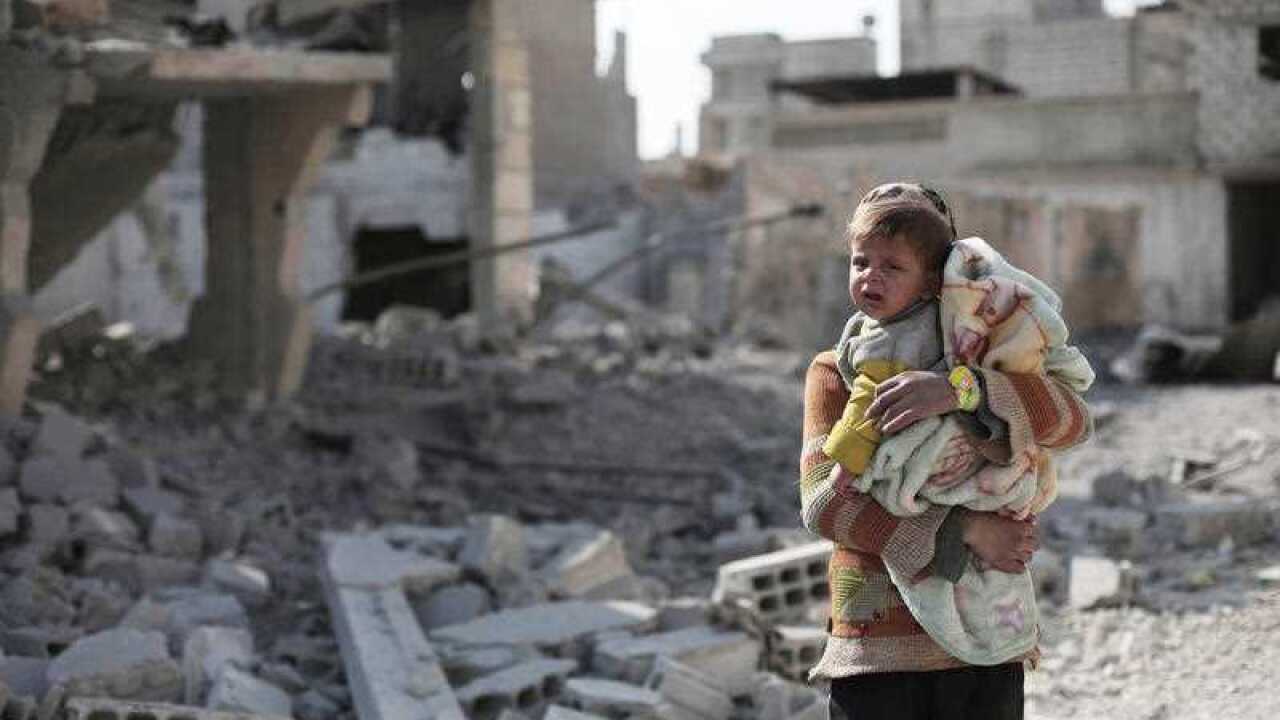 A girl carries a baby past some bombed out ruins in Eastern Ghouta, Syria.