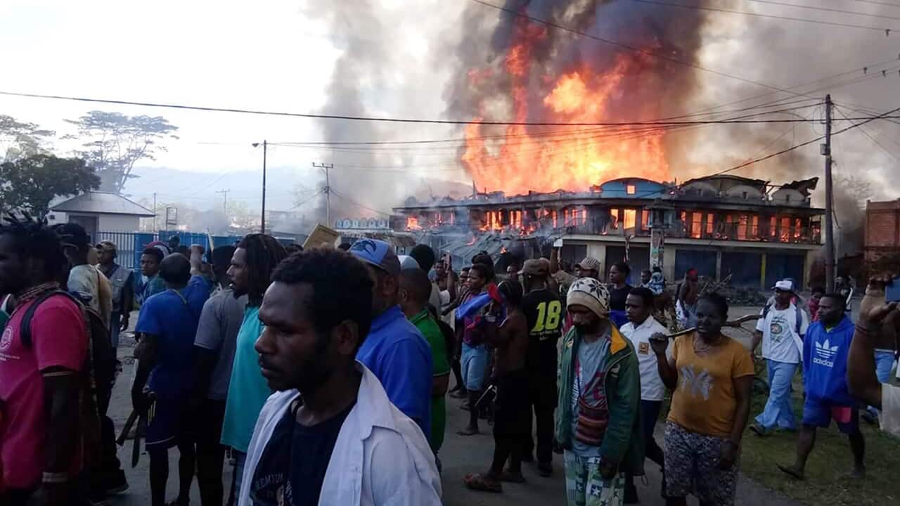 People gather as shops burn in the background during a protest in Wamena on 23 September.