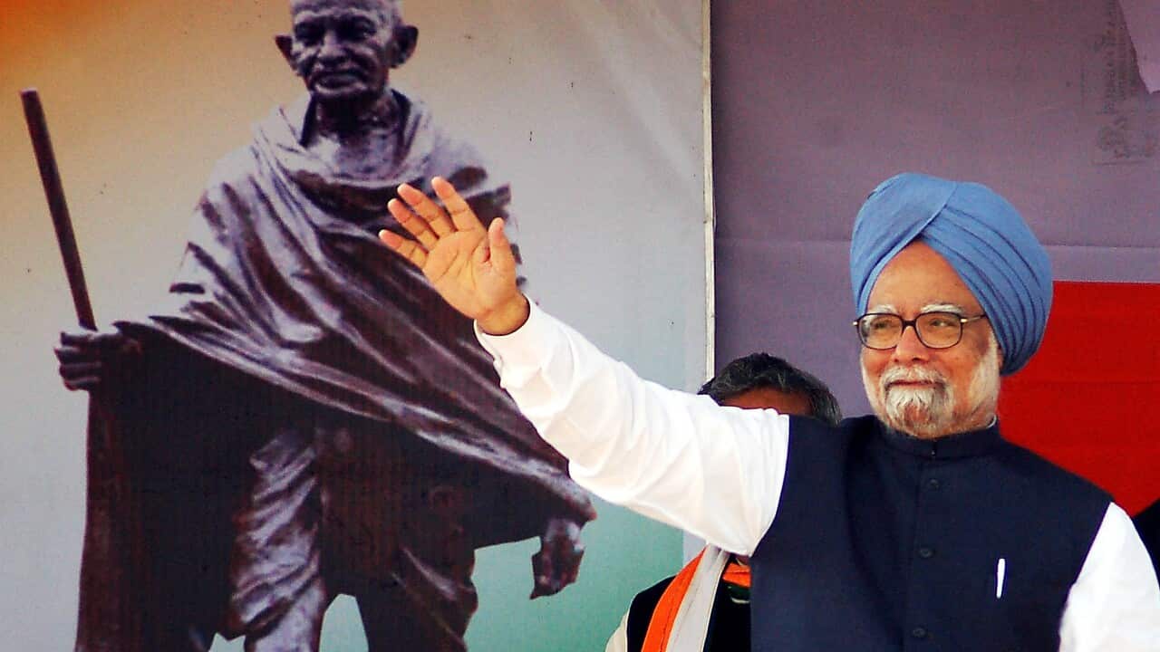 A man wearing a blue turban waves at a crowd in front of a Mahatma Gandhi poster.