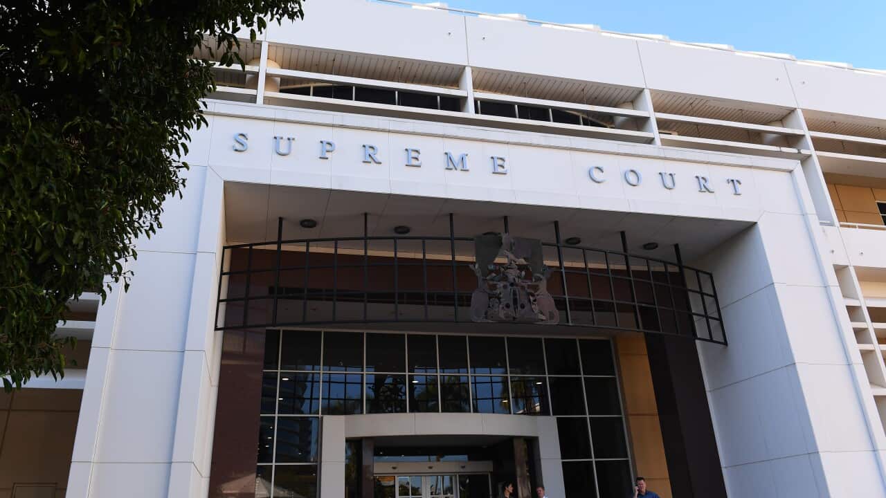 A low-angle exterior shot of a modern, white building with the words "SUPREME COURT" in silver lettering above the entrance, with a tree branch partially obscuring the left side.