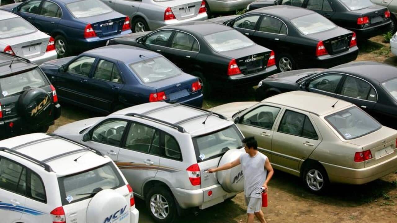 A man opens the back door to a vehicle on a car lot.