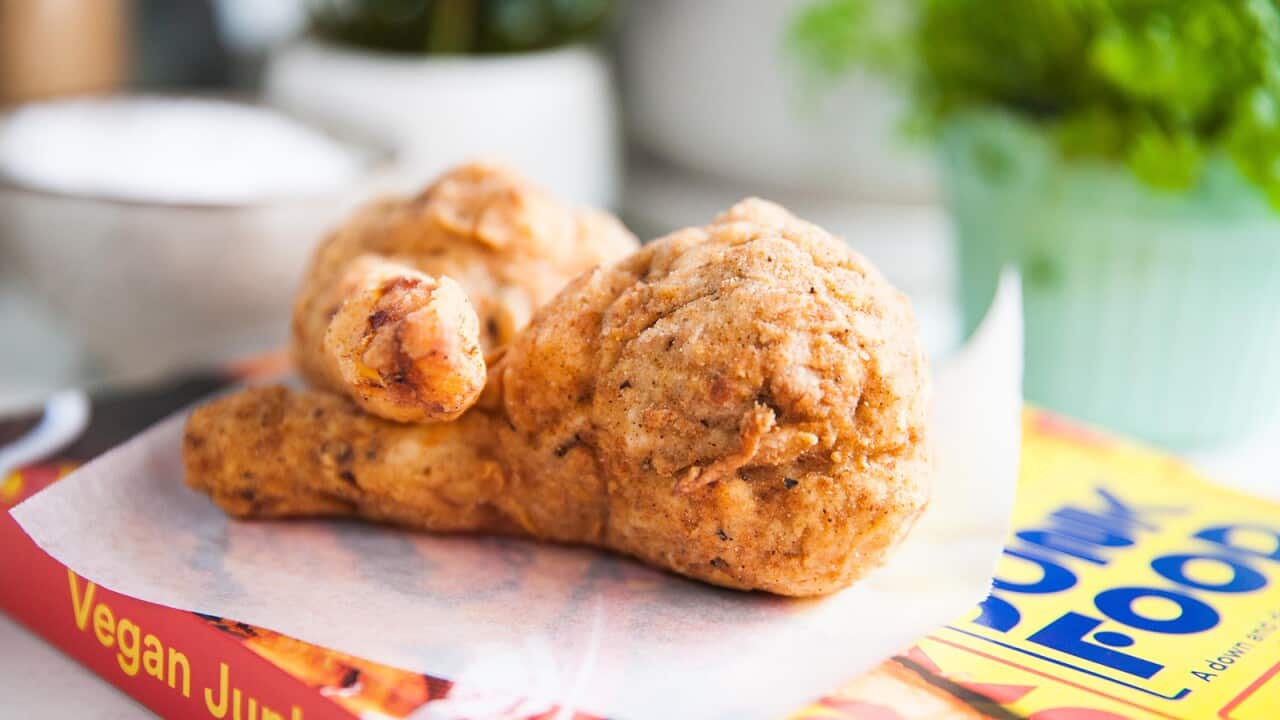 Two drumstick shapes sit on a piece of baking paper, on top of a colourful book. The title Vegan Junk Food can be seen on the spine.