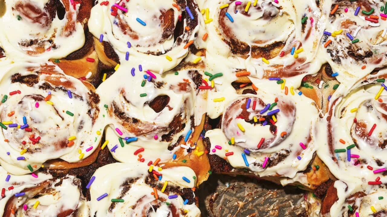 A tray of bun scrolls, with white icing and colourful sprinkles, is seen from overhead.
