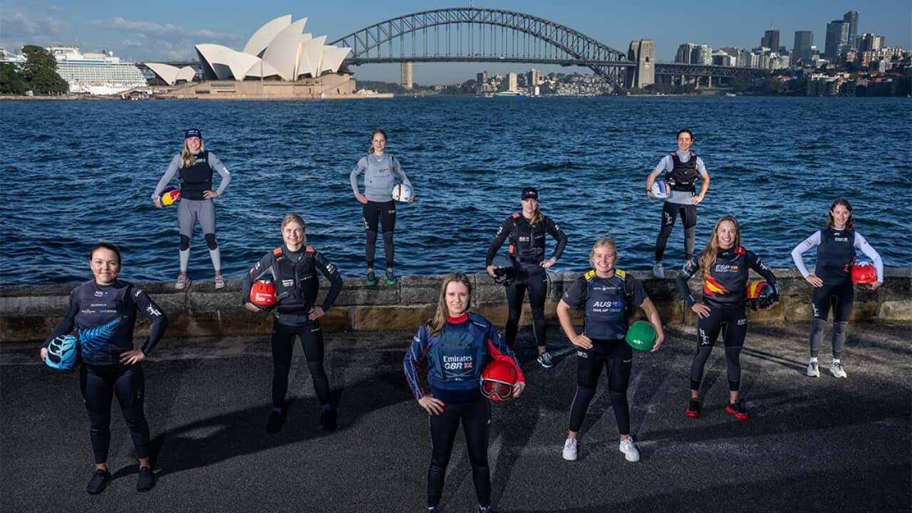 Female sailors competing in SailGP Sydney are seen with their head safety equipment in front of a view of the Opera House and Sydney Harbour Bridge.