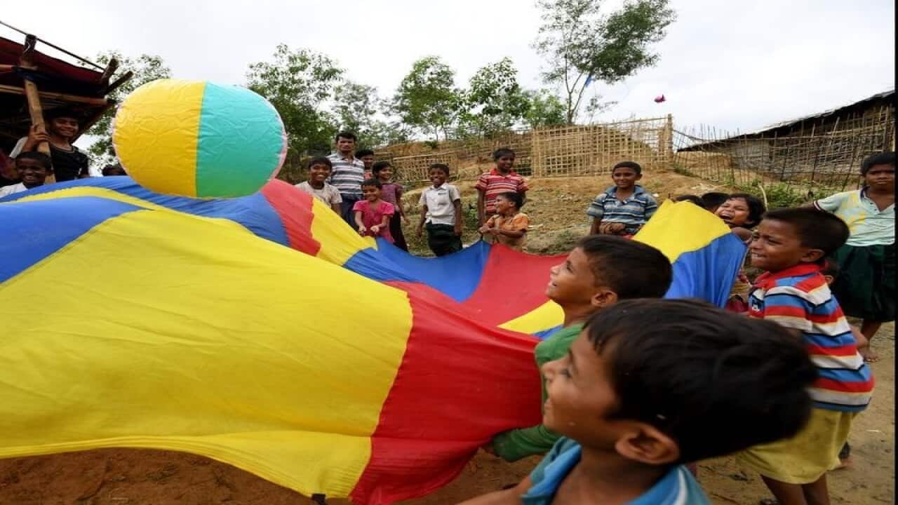 Rohingya children play with a ball on a multicoloured sheet.