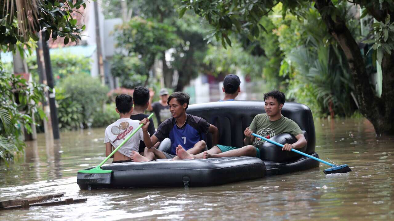 Residents paddle through a flooded neighbourhood outside Jakarta