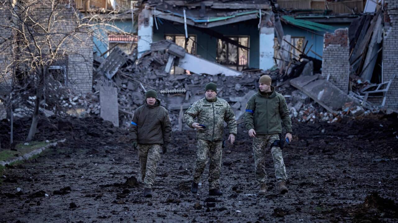 Three Ukrainian soldiers in front of destroyed buildings in the Donbas region.