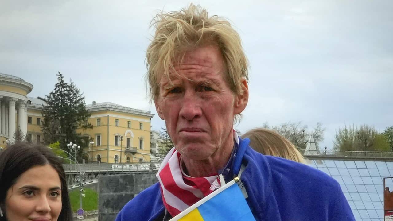 A man holding a Ukraine flag wearing an American flag around his neck