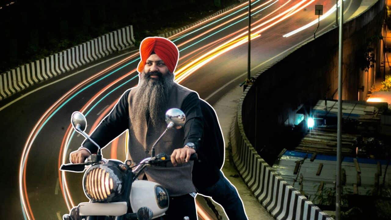 A sikh rider driving a Royal Enfield bike on a flyover with lights in the background representing speed and movement.