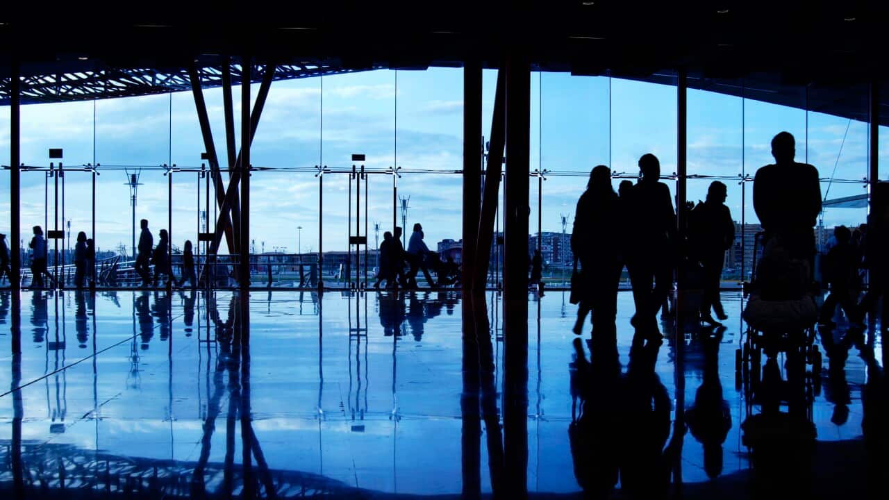 Several travellers are seen milling about in an dimly lit airport terminal.