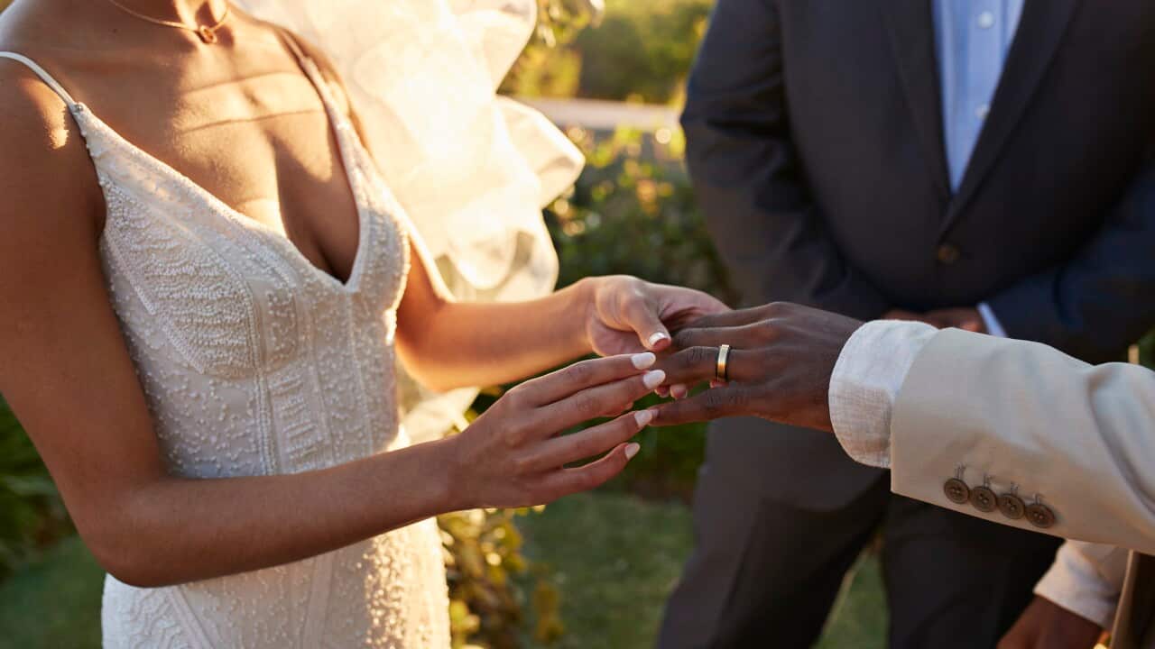 Midsection of young bride exchanging wedding ring with groom while holding hands during ceremony at sunset