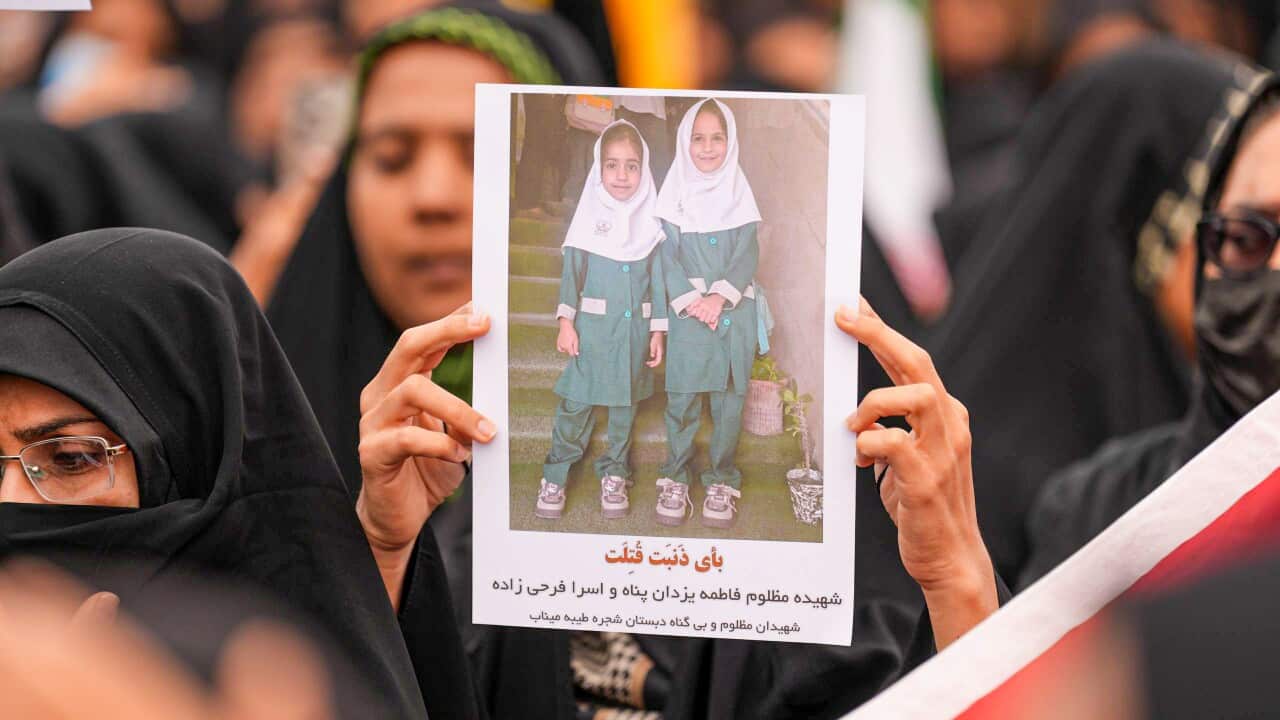 A woman standing in a crowd holds a photo of two young girls in school uniform