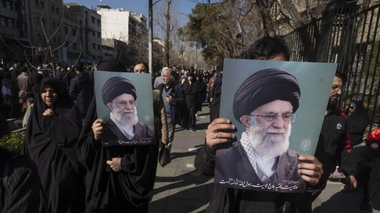 People in a crowded outdoor walkway carry large portraits of Iranian Supreme Leader Ali Khamenei during a public gathering.