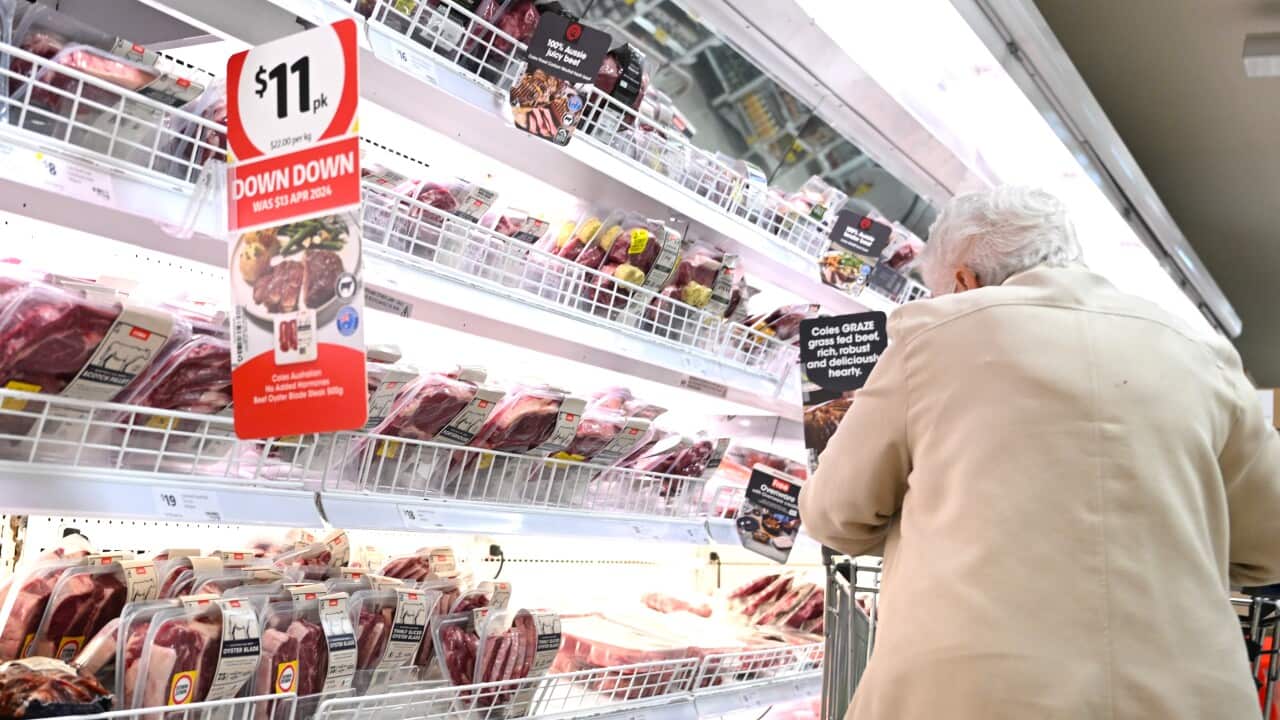 An elderly woman with a shopping trolley looking at the meat section at a Coles supermarket