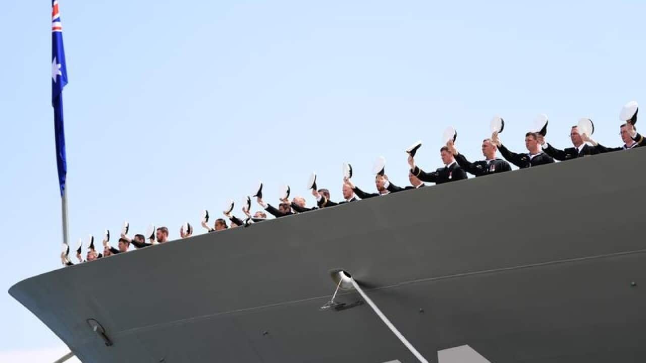 The crew of HMAS Hobart raise their hats to cheer the ship.