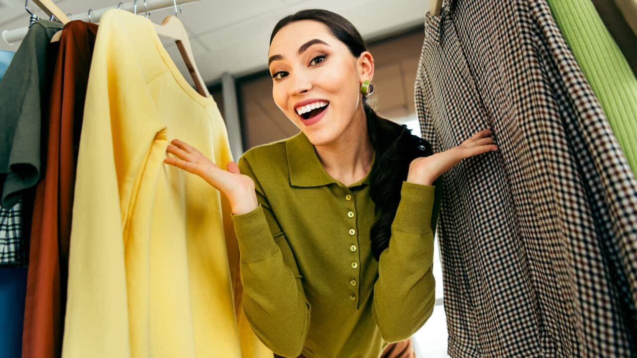 Confident young designer showcasing clothing collection in her stylish workspace, highlighting textiles, fashion, and creativity
