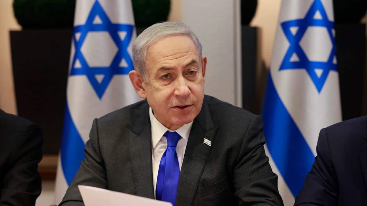 Israel's Prime Minister Benjamin Netanyahu chairing a meeting. Behind him are two Iraeli flags on flagpoles