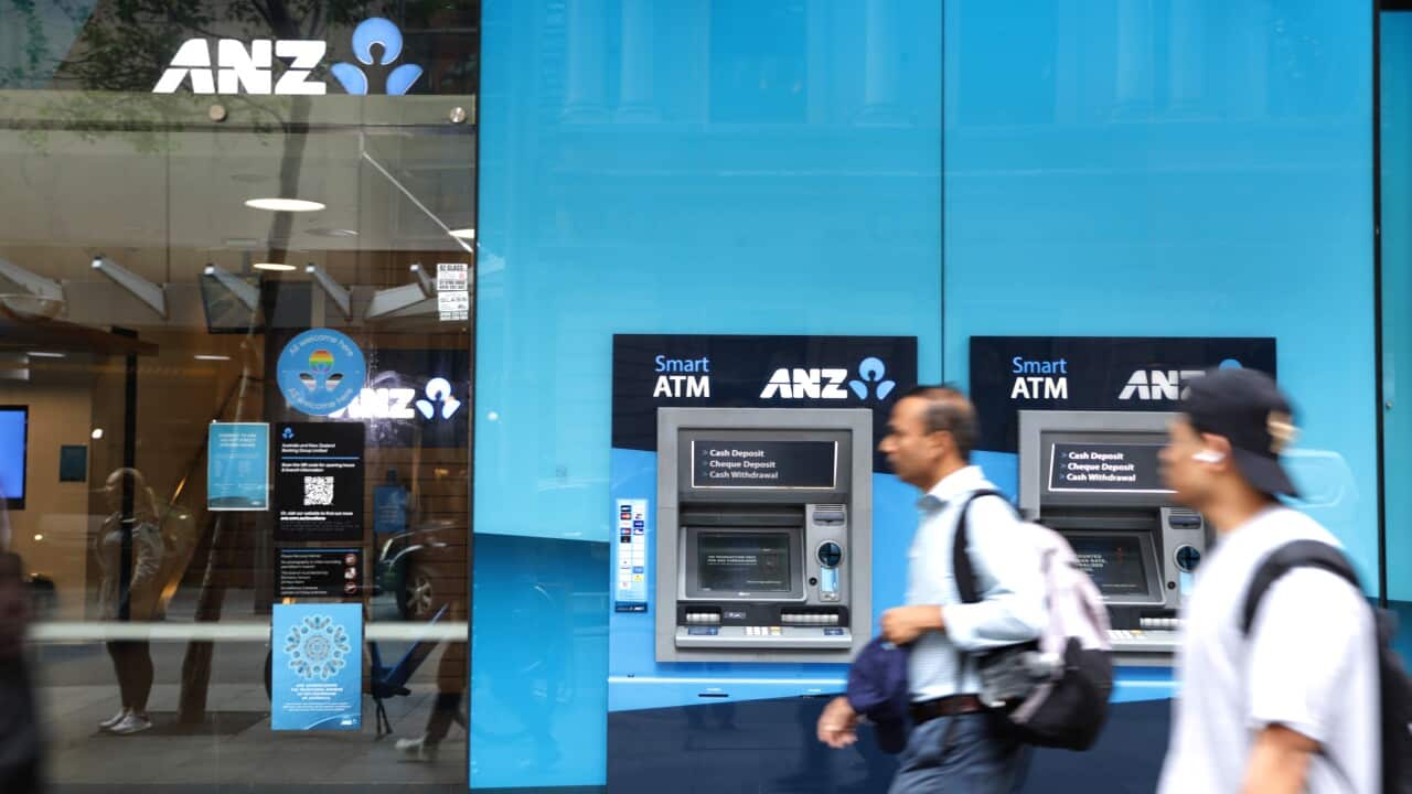 Two people walk past a blue building with ANZ signs displayed