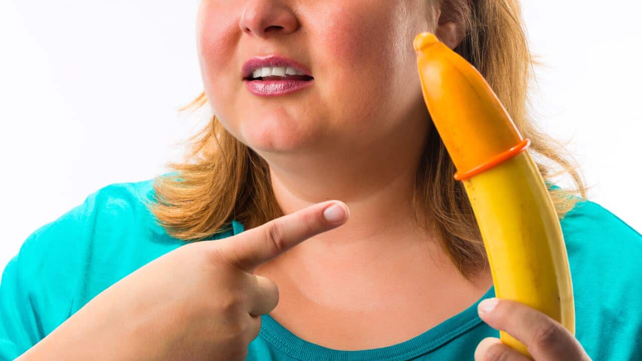 Young woman holding  banana with condom - she looks confused