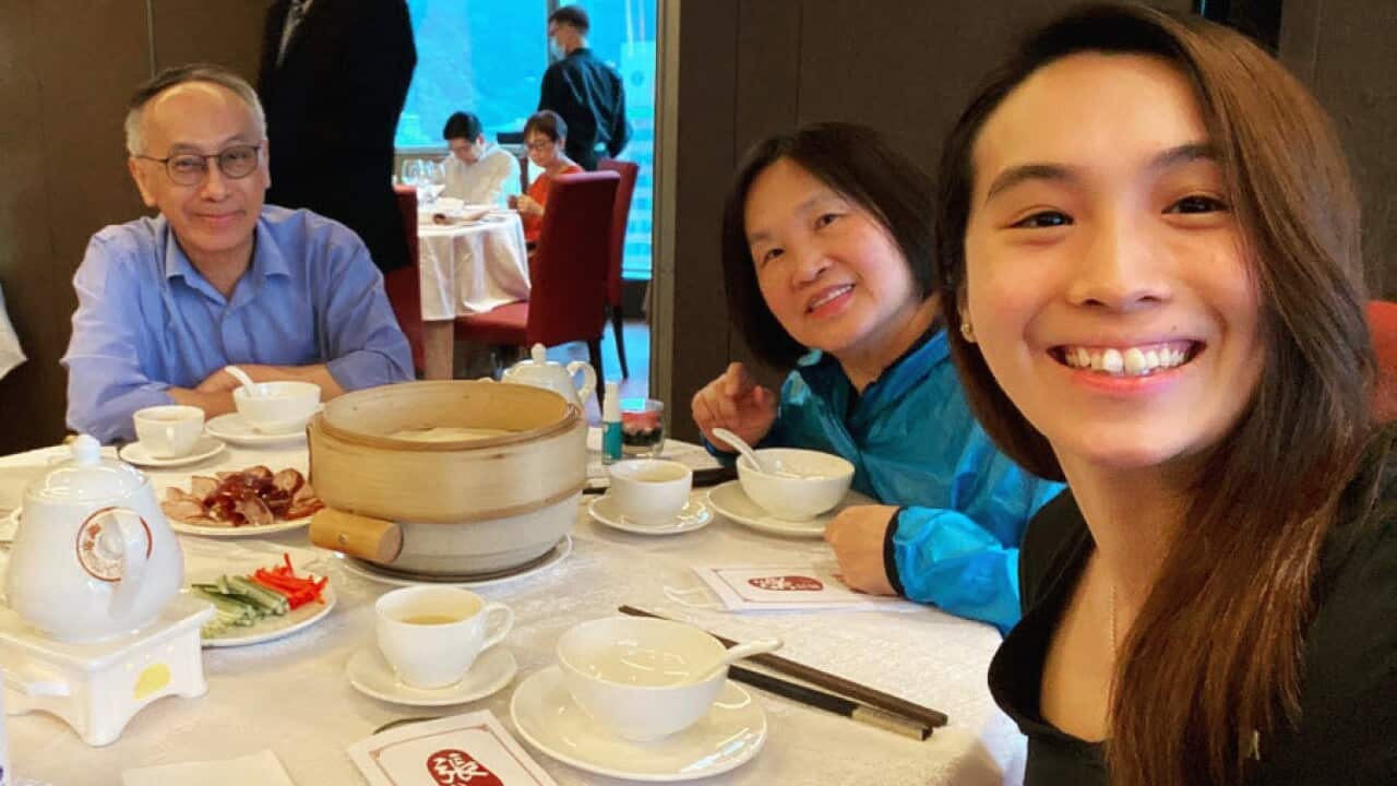 A young Asian woman with her parents, smiling as they enjoy a meal together at a restaurant.